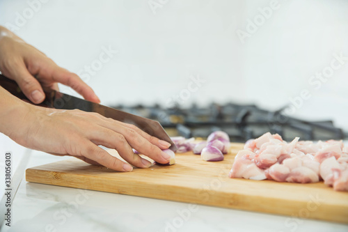 Woman cutting raw meat on wooden board in kitchen. Female hands with a knife in their hand cut fresh meat on a table.