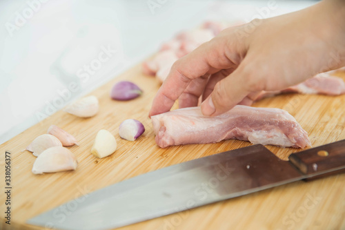 Woman cutting raw meat on wooden board in kitchen. Female hands with a knife in their hand cut fresh meat on a table.