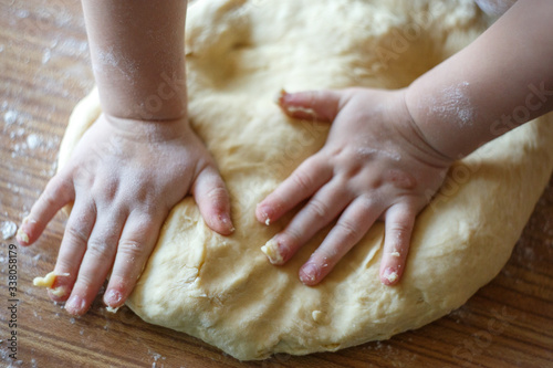 Child's hands knead yeast dough closeup