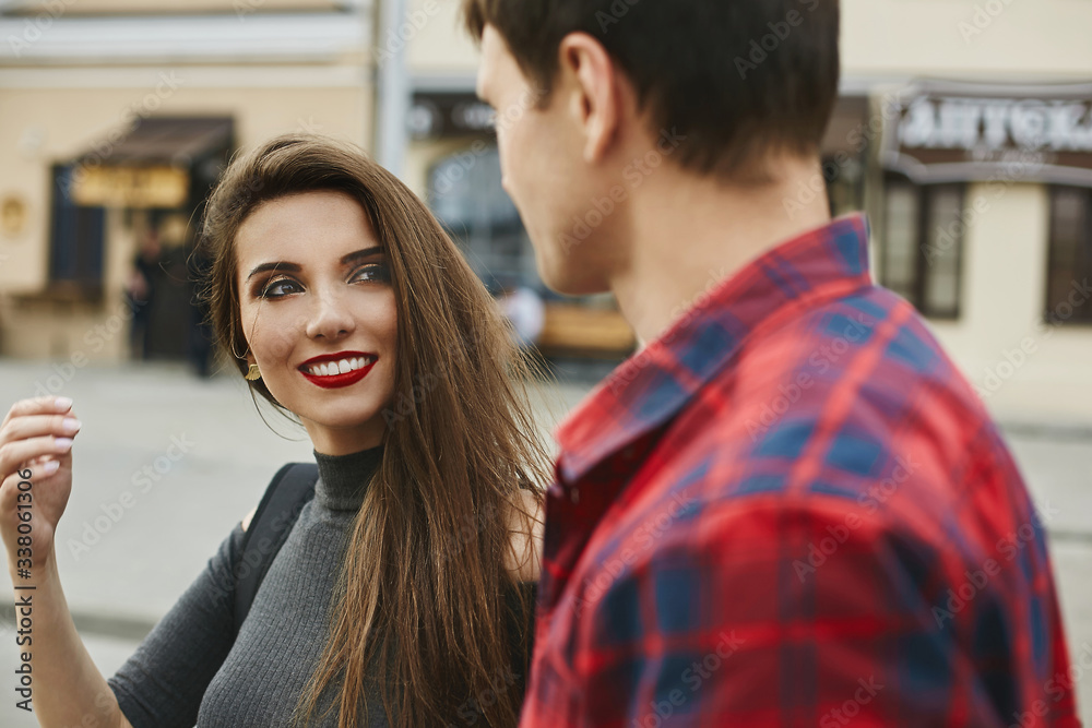 Young beautiful couple of lovers at the dating. Young woman with a perfect white smile and red lips and a handsome young man spending time together in the city Young beautiful couple of lovers at the dating. Young woman with a perfect white smile and red lips and a handsome young man spending time together in the city