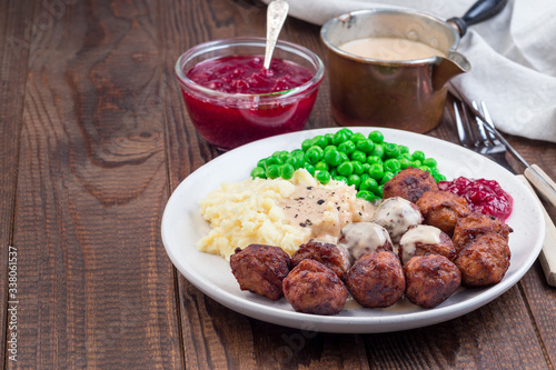 Traditional swedish meatballs served with mashed potato, green peas, cream sauce and cranberry jam, on plate, horizontal, copy space