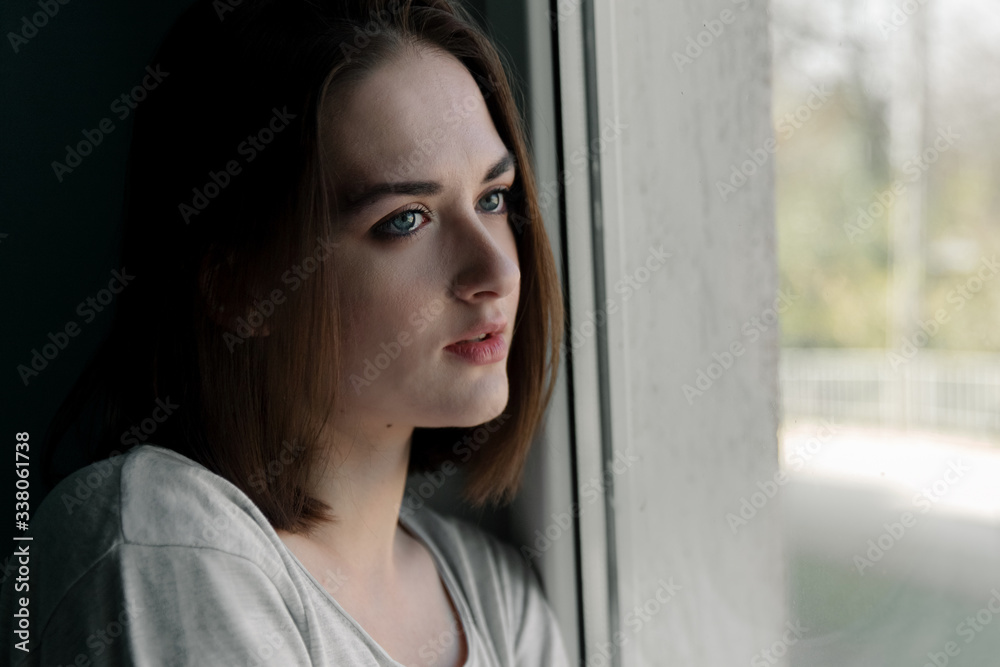 The girl is sad in the house by the window in self-isolation The girl is sad in the house by the window in self-isolation