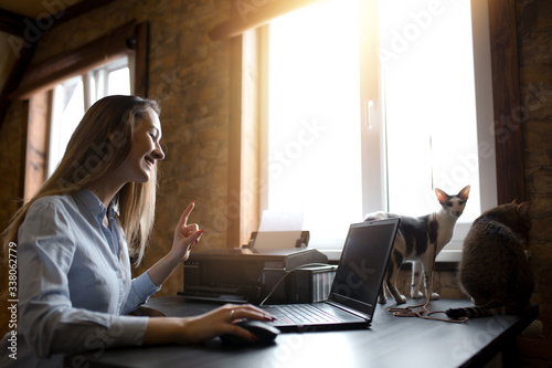 A young girl working remotely and talking with clients on marketing forecasting. Oriental breed of cat.