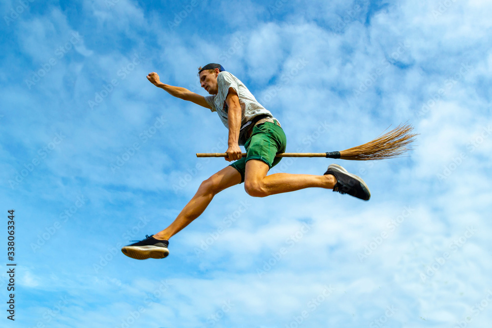 Young man flying on the broom with outstretched arm in the blue sky of Siquijor Young man flying on the broom with outstretched arm in the blue sky of Siquijor