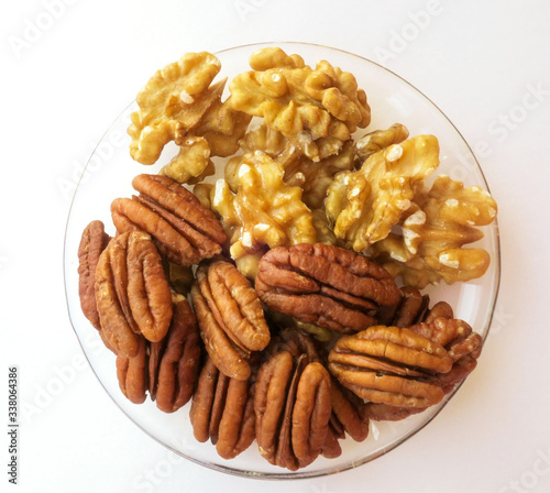Pecans and walnuts in a glass plate on a light background