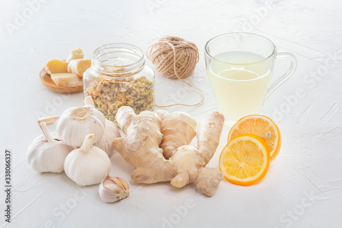 Ginger, garlic, lemon, dried medical chamomile in a jar and ginger tea - a means to protect against viral infections and colds on a light wooden table.