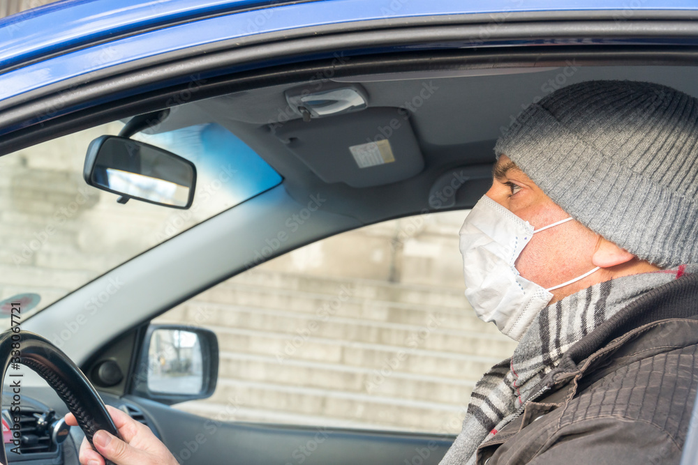 Man behind the wheel covering his face with a medical mask to protect his nose and mouth Man behind the wheel covering his face with a medical mask to protect his nose and mouth