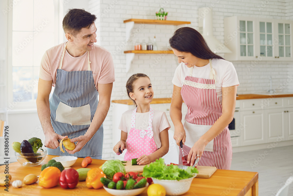 Happy family with kid preparing fresh vegetables on the table in the kitchen.