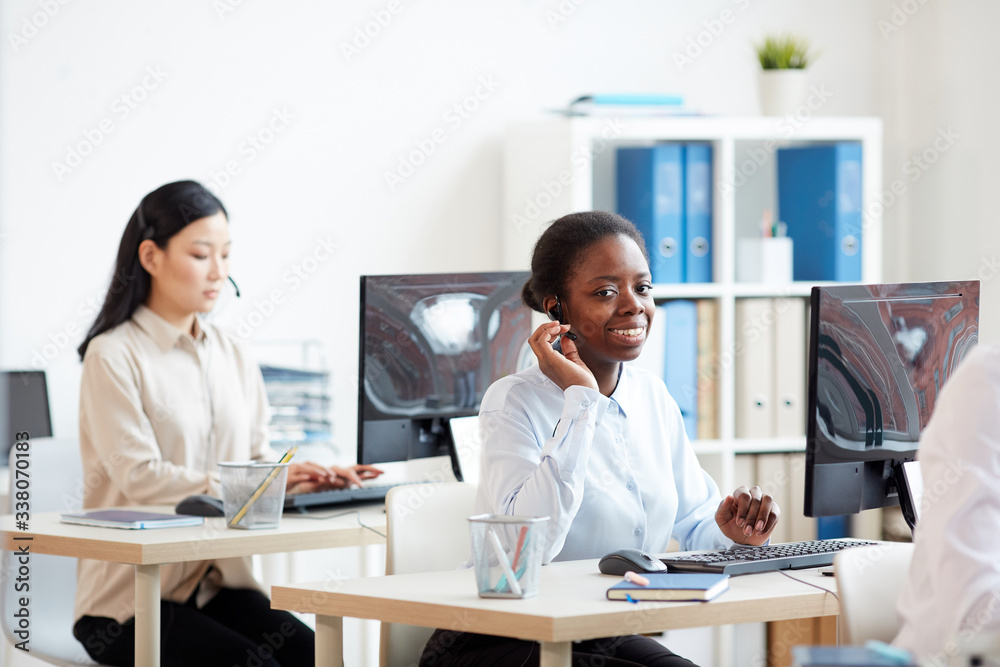 Portrait of smiling African-American woman wearing headset and talking to customer while working in support call center, copy space Portrait of smiling African-American woman wearing headset and talking to customer while working in support call center, copy space