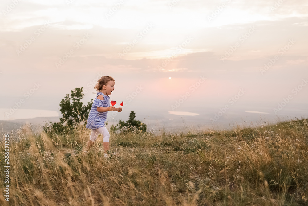 A girl runs through a clearing at sunset. A girl in a striped t-shirt and leggings. Blonde girl with lollipops on a stick in nature.