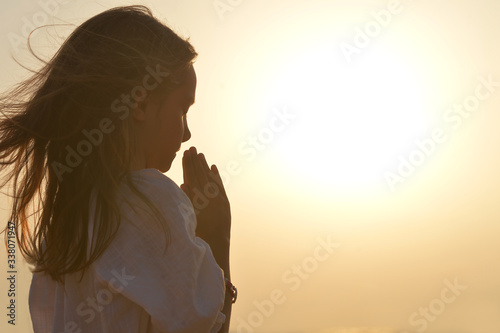Portrait of little girl praying on light background photo