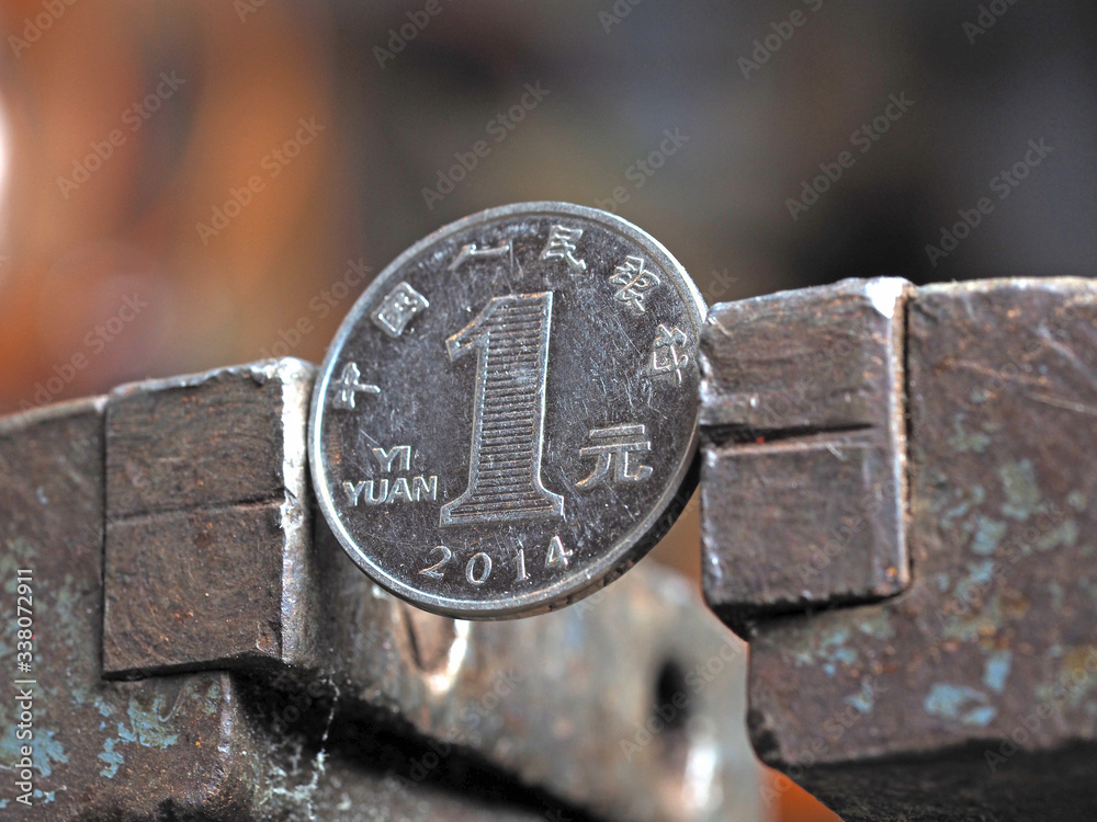 Yuan coin clamped in a metal vise. Currency under the onslaught, the concept of financial problems and crisis Yuan coin clamped in a metal vise. Currency under the onslaught, the concept of financial problems and crisis