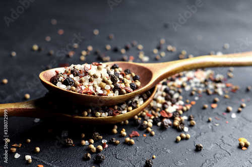 Spoons with multicolored spices on dark slate background - peppers mix, sea salt, cardamon, mustard seeds and paprika flakes.
