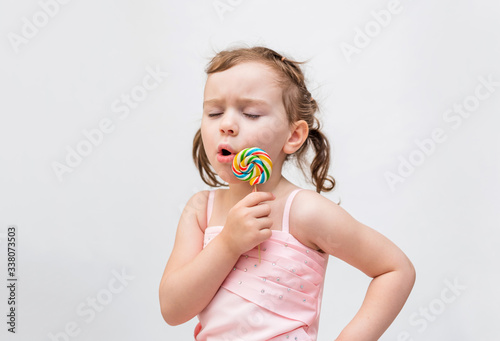 On white background with copy space.Cute girl with pigtails on a white background in a pink dress. A blonde girl with a Lollipop. The girl has a toothache.
