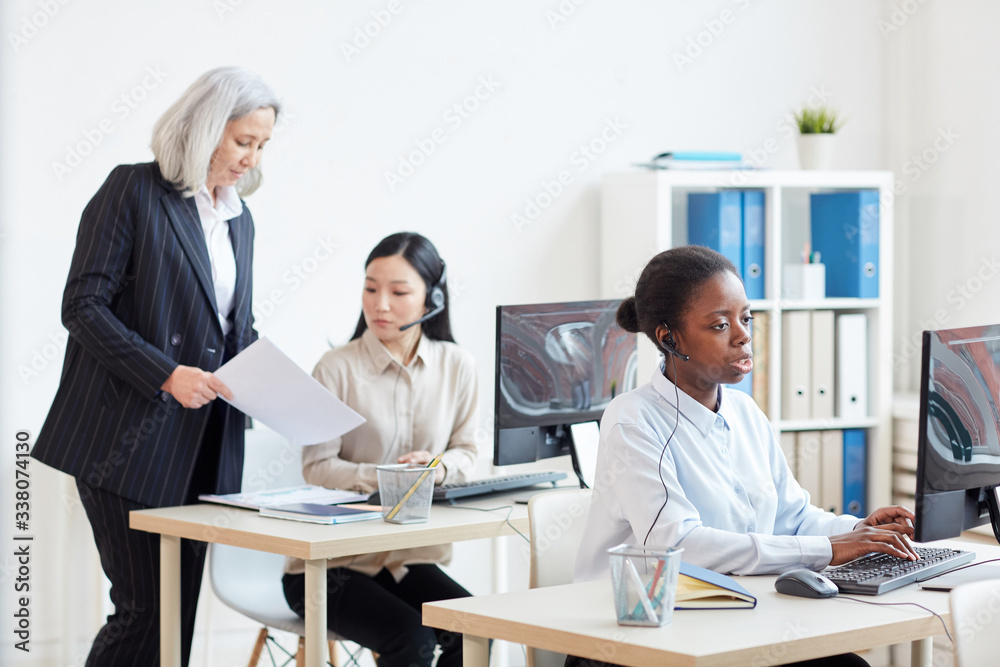 Portrait of senior businesswoman supervising call center operators in white office interior, copy space Portrait of senior businesswoman supervising call center operators in white office interior, copy space