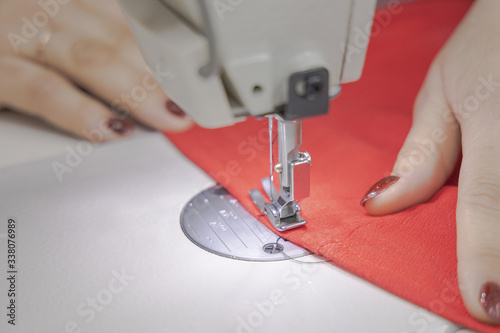 The master sews on a sewing machine. The master is sewing red fabric on a sewing machine. Closeup