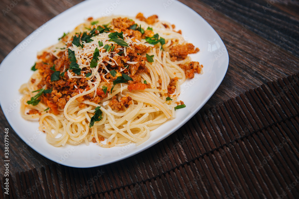 Spaghetti with minced meat in tomato with herbs and cheese on a white plate. Plate with food on a dark wooden table. Lunch with meat. Spaghetti with minced meat in tomato with herbs and cheese on a white plate. Plate with food on a dark wooden table. Lunch with meat.