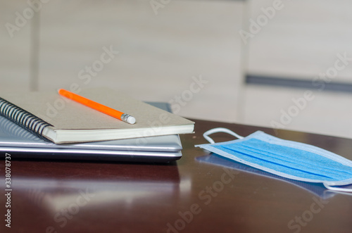 Laptop and a notebook on a wooden table And a mask The concept of working at home during the introvert to prevent the Covid-19 virus