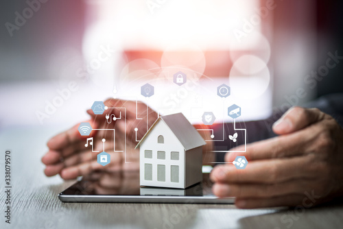 Small house model is on tablet with man's hand and icons home electronics devices connecting with wireless.