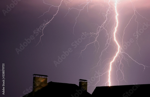 a powerful bolt of lightning in the night sky against the background of house roofs