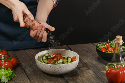 Woman salting fresh healthy vegetable salad on wooden table. Female hands with copyspace.