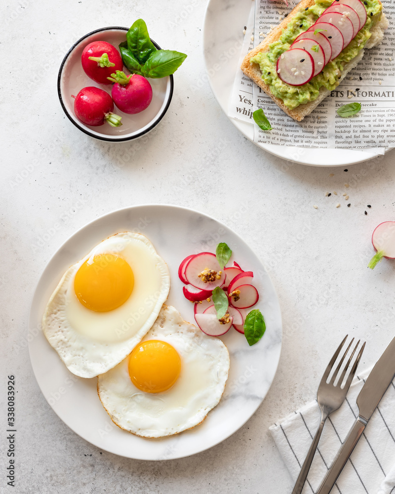 top view of a healthy easy breakfast of fried eggs and toast with mashed avocado, radish and sesame seeds. light concrete background. vertical image