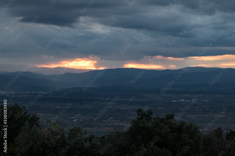Lumière orangée du coucher de soleil traversant un ciel très nuageux et menaçant au dessus des montagnes des Cévennes (Occitanie, France) Lumière orangée du coucher de soleil traversant un ciel très nuageux et menaçant au dessus des montagnes des Cévennes (Occitanie, France)