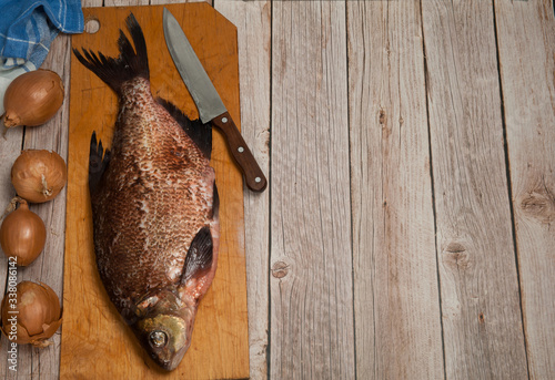 Cooking fresh river fish.Peeled fish-bream (Abramis), with a bow and knife lies on a cutting board on a wooden background. Free space.