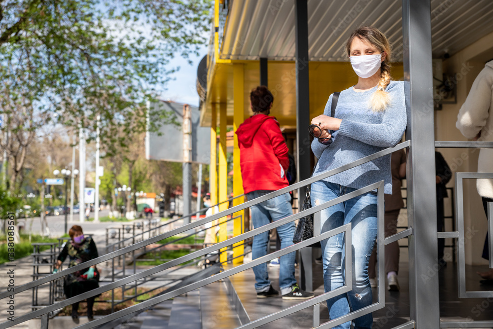 young woman standing in line at the market. in a protective mask during a coronovirus pandemic. dressed in a blue sweater and jeans. blonde with gathered hair. Coronavirus pandemic effects.
