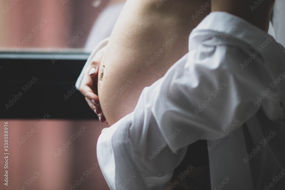 Cute naked pregnant belly. The girl is standing near the window.