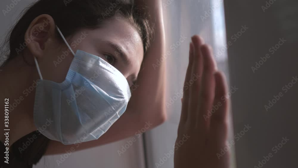 little girl looks out the window sad in a medical gauze mask lifestyle ...