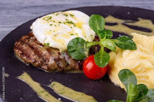 A piece of steak with egg paschot  served with puree potatoes and cherry tomatoes with greens