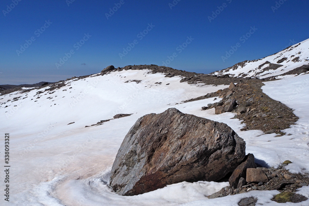 The mountain landscape with the big rock on foreground, rocks covered by white snow, the clean blue sky.