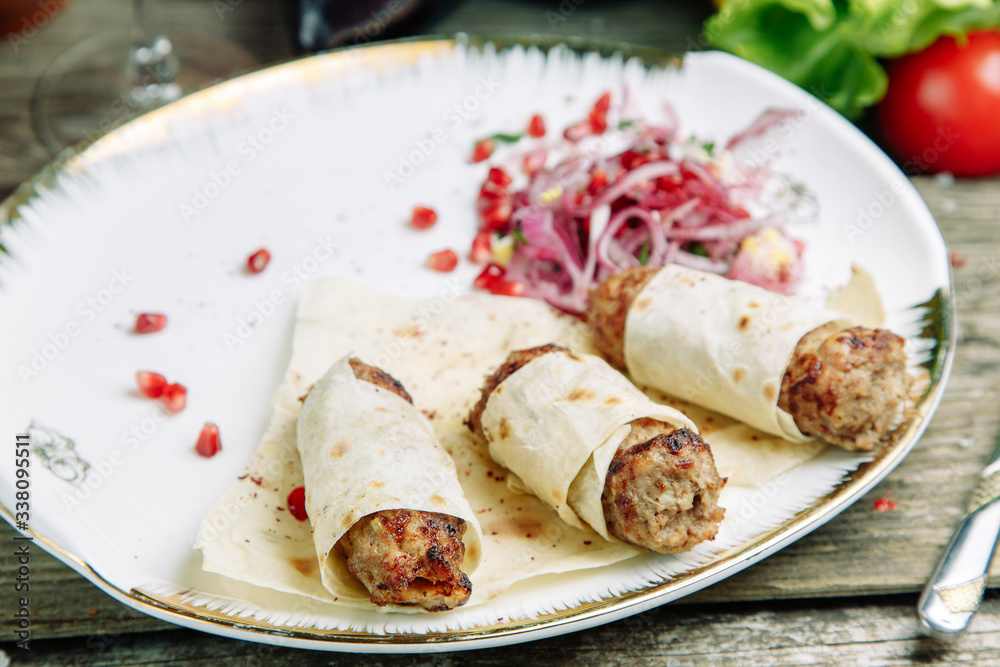 Restaurant dish on a wooden background with vegetables. Lula kebab in lavash with pomegranate and onion on a plate. Restaurant dish on a wooden background with vegetables. Lula kebab in lavash with pomegranate and onion on a plate.