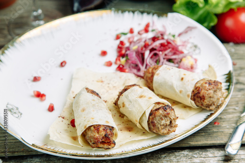 Restaurant dish on a wooden background with vegetables. Lula kebab in lavash with pomegranate and onion on a plate.