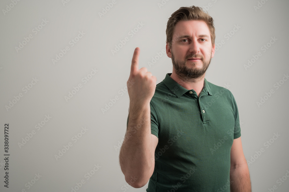 Portrait of serious stylish attractive man with thick beard, dressed in casual green t shirt showing number one Portrait of serious stylish attractive man with thick beard, dressed in casual green t shirt showing number one