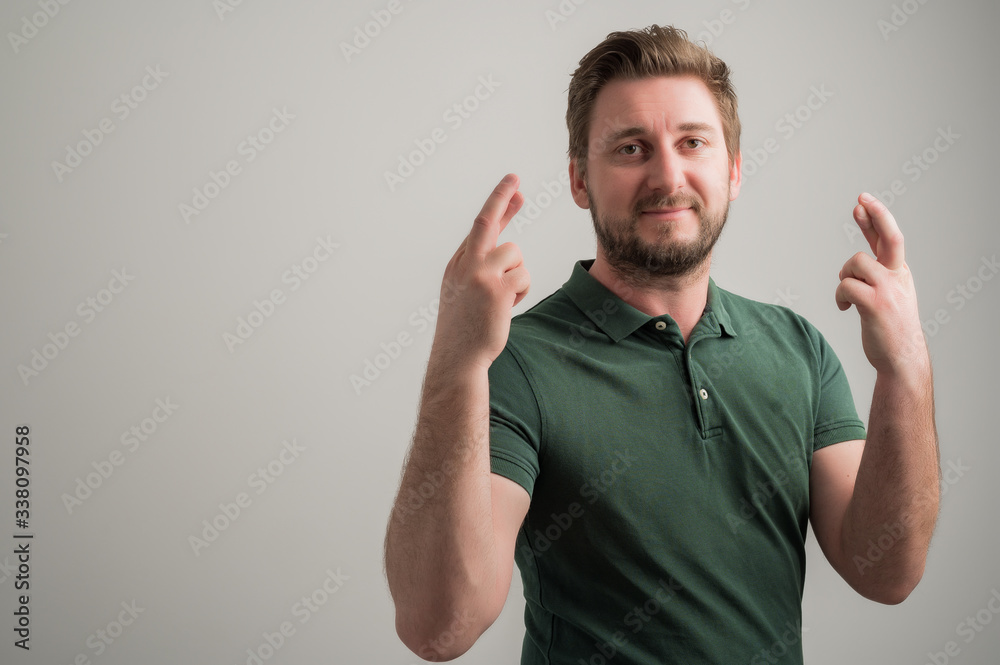 Portrait of serious stylish attractive man with thick beard, dressed in casual green t shirt showing double fingers crossed Portrait of serious stylish attractive man with thick beard, dressed in casual green t shirt showing double fingers crossed