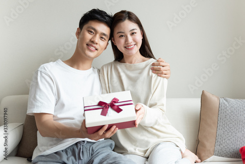 A young Asian couple giving each other gifts on the sofa