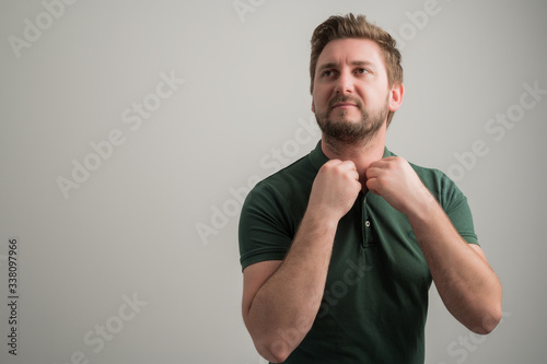 Portrait of serious stylish attractive man with thick beard, dressed in casual green t shirt, arranging t shirt coller