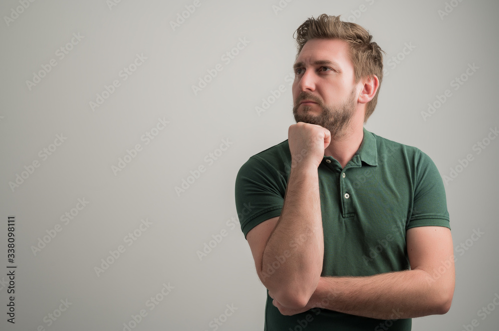 Portrait of serious stylish attractive man with thick beard, dressed in casual green t shirt making thinking gesture hand under chin Portrait of serious stylish attractive man with thick beard, dressed in casual green t shirt making thinking gesture hand under chin