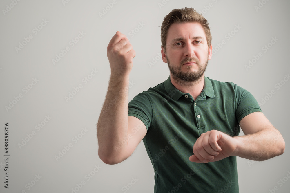 Portrait of serious stylish attractive man with thick beard, dressed in casual green t shirt showing time is money gesture Portrait of serious stylish attractive man with thick beard, dressed in casual green t shirt showing time is money gesture