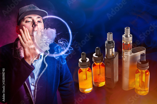 Vapes and vials with liquids on the background of a Vaper. A man in a baseball cap blows vape smoke. Smoke from a VAPE in the form of a circle. Smoking electronic cigarettes.