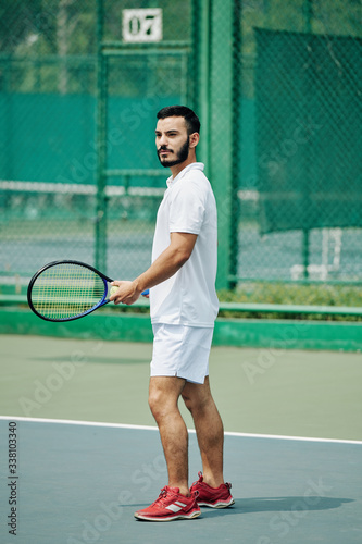 Handsome young Hispanic man in white sports clothing playing tennis outdoors © DragonImages