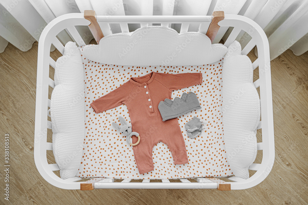 White wooden baby crib with pillows shaped clouds in baby s room. Newborn clothes and accessories in cot. Top view of child s bed Stock Foto Adobe Stock