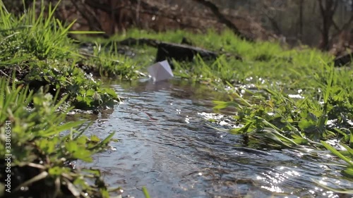 Paper ship. A paper boat is floating on the water. White paper ship. A boat  floats on water. A paper boat is floating on the river. Forest river. River runs along a forest.