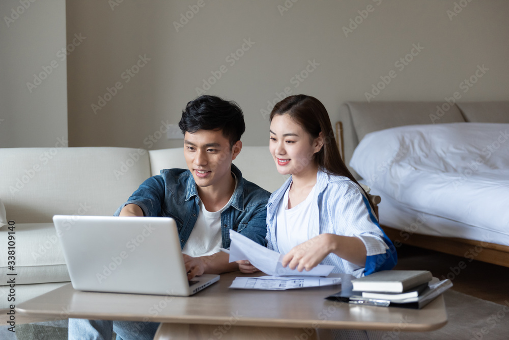 A young asian couple is sitting on a carpet using a computer A young asian couple is sitting on a carpet using a computer