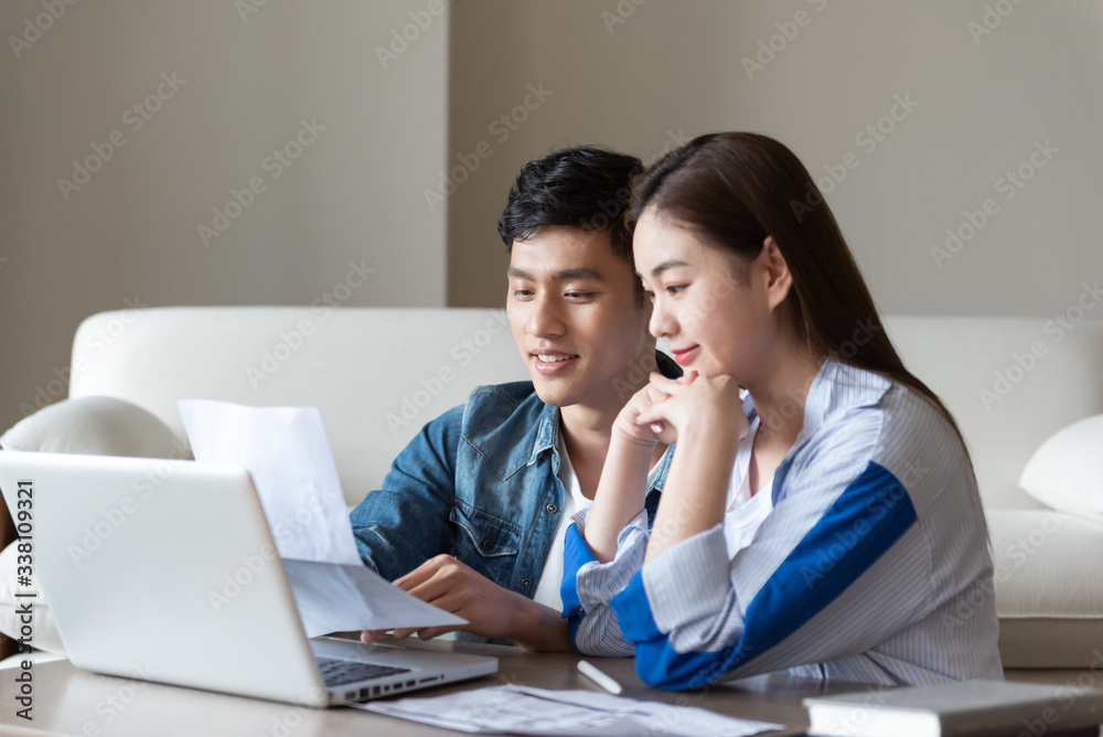 A young asian couple is sitting on a carpet using a computer A young asian couple is sitting on a carpet using a computer
