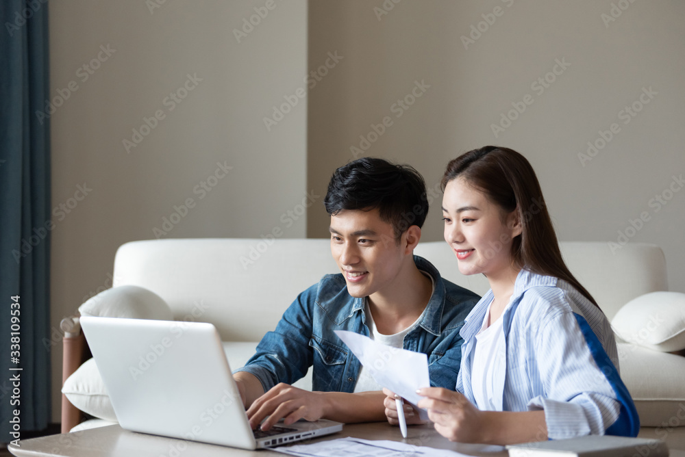 A young asian couple is sitting on a carpet using a computer A young asian couple is sitting on a carpet using a computer