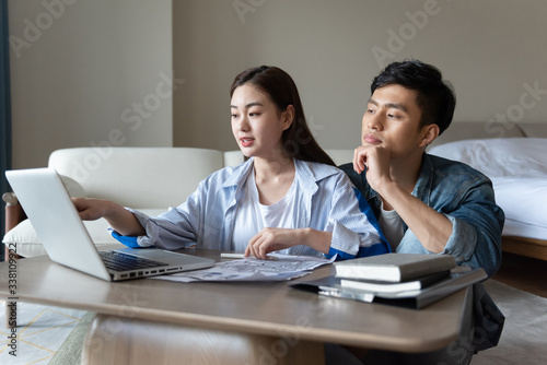 A young asian couple is sitting on a carpet using a computer