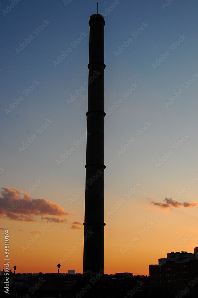 old industrial chimney silhouetted against an orange sunset sky